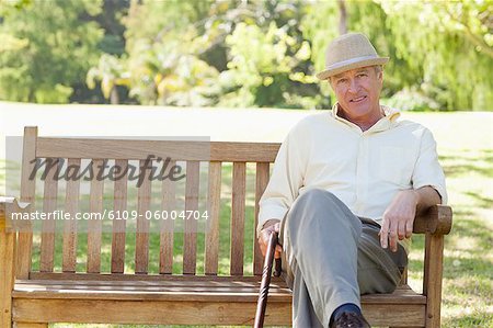 Man holding a cane and sitting on a bench while he looks ahead of him in a park