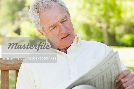 Man concentrating while reading a newspaper in a park