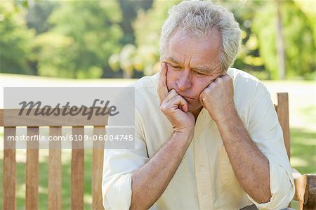 Man resting his face between his hands as he sits on a bench in a park