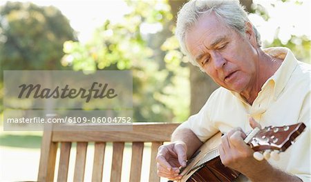 Ein Lied singen, während Sie spielen auch eine Gitarre, als er auf einer Bank im Park sitzt man