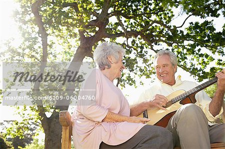 Mann, seine Gitarre zu spielen, für seinen Freund, der neben ihm auf einer Bank sitzt