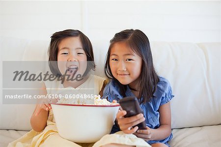 Two laughing sisters watching tv together with a bowl of popcorn and the tv remote