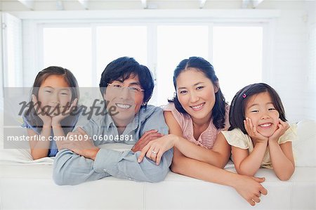 La famille souriant comme ils s'agenouillent sur le canapé ensemble