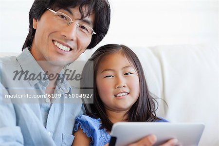 A close up shot of a smiling dad and his daughter using a tablet together on the couch