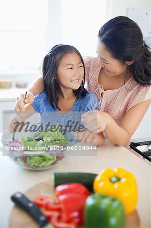 Une fille sourit à sa mère qu'ils sont assis dans la cuisine, jetant une salade ensemble