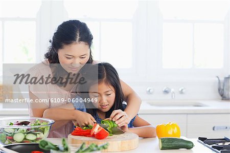 Mutter und Tochter sorgfältig schneiden Paprika mit einem Messer in der Küche.