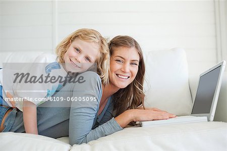 Une mère et son fils que tous les deux se trouvent sur le canapé avec un ordinateur portable comme ils regardent vers l'avant et sourire