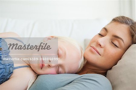 A son lying on top of her mother as they both lie across the couch sleeping
