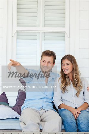 Un homme souriant et une femme assis ensemble à l'extérieur comme l'homme montre la femme quelque chose au loin