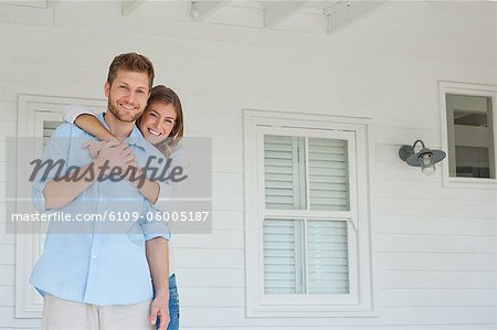 A smiling wife holding onto her husband as they stand on the porch while looking forward