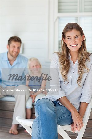 The focus is on the woman sitting by herself as the husband and daughter sit in the background