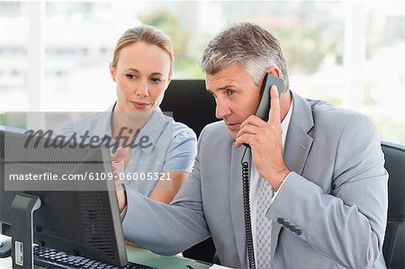 Boss on the phone while an employee is next to him in a bright office