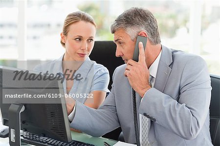 Boss on the phone while an employee is next to him in a bright office