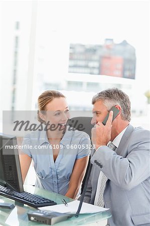 Chef am Telefon während lächelnd an einen Mitarbeiter in einem hellen Büro