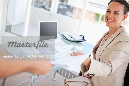 Geschäftsfrau mit einem Zopf geben eine Datei an jemanden in einem hellen Büro