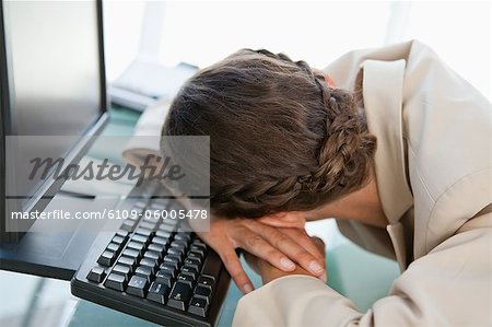 Geschäftsfrau mit Geflecht Kopf auf der Tastatur in einem hellen Büro