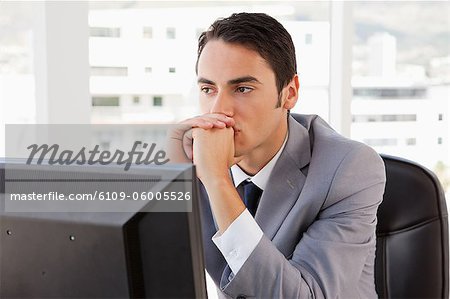 Homme d'affaires pensant devant son ordinateur dans un bureau lumineux