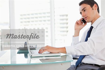 Homme d'affaires appelant tout en cliquant sur son ordinateur portable dans un bureau lumineux