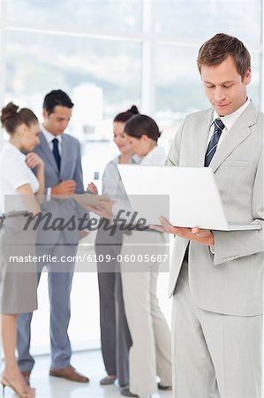 Young salesman with his laptop and colleagues behind him