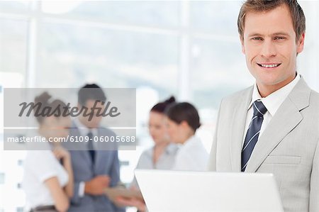 Smiling young salesman with notebook and colleagues behind him