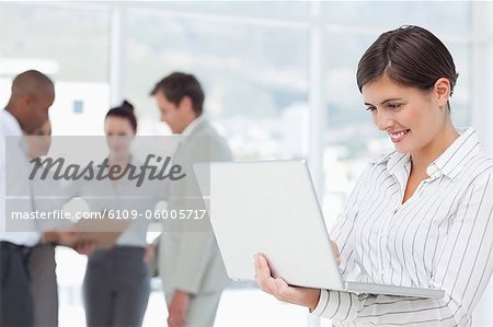 Junge Verkäuferin auf ihrem Laptop Lächeln mit Kollegen hinter ihr