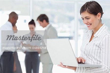 Junge Verkäuferin mit Laptop und Kollegen hinter ihr Lächeln