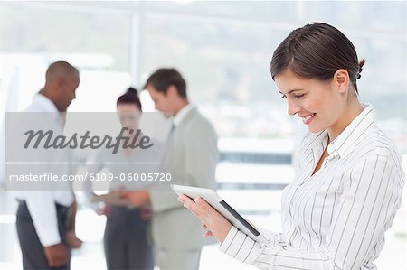Junge Verkäuferin mit ihrem Tablet PC und Kollegen hinter ihr Lächeln