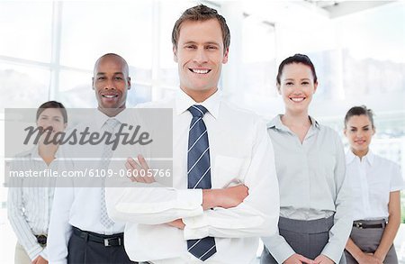 Smiling young businessman with arms crossed and his team