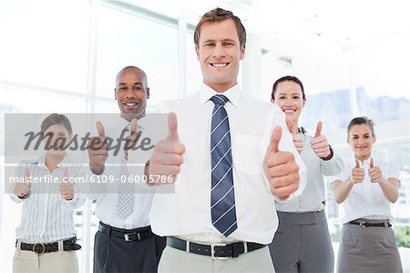 Smiling businessman and his team giving thumbs up