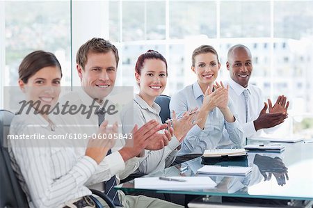 Side view of applauding young salesteam sitting at a table