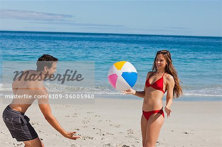Couple attrayant jouant sur la plage avec un ballon