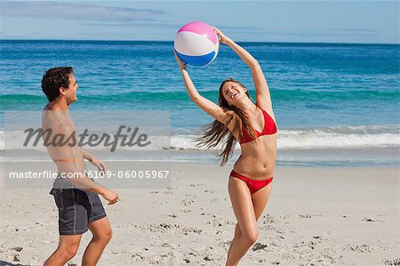 Attractive woman playing with a ball in front of her boyfriend on the beauch