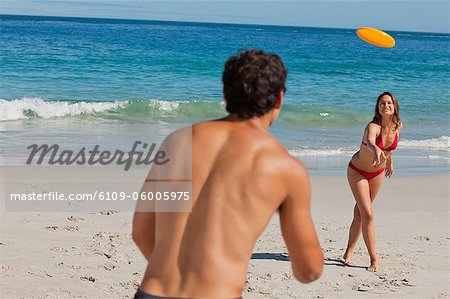 Attractive couple playing with a Frisbee on the beach with sea in background