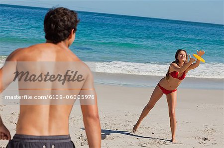 Frau Fang ein Frisbee am Strand mit ihrem Freund im Vordergrund und das Meer im Hintergrund