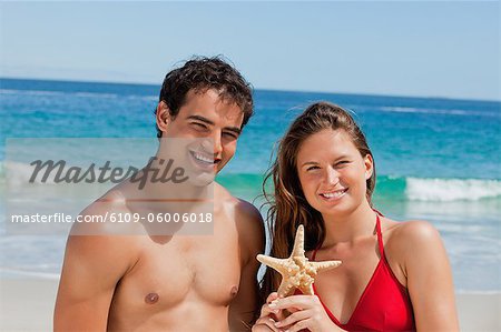 Portrait of a couple holding a starfish with the sea in background