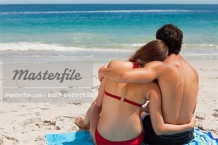 Rear view of a lovers sitting on beach towel in front of the sea