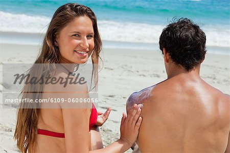 Portrait of a woman applying sunscreen on the shoulder of her boyfriend in front of the sea