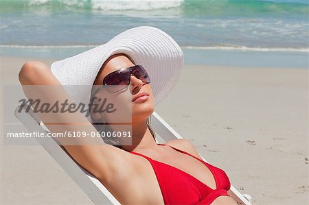 Pretty woman on a deck chair with sunglasses having a sunbath with the sea in background