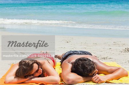 Bronzée couple dormir sur la plage avec la mer en arrière-plan