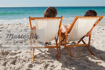 Rückansicht des Menschen im Badeanzug, nehmen ein Sonnenbad auf den Liegestühlen vor dem Ozean