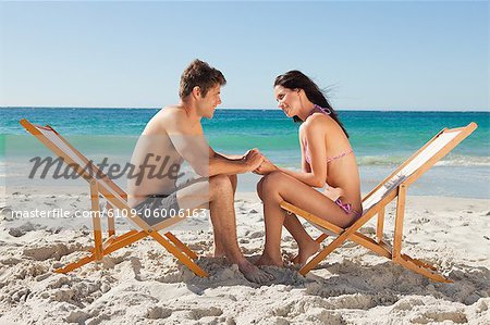 Paar im Badeanzug von Angesicht zu Angesicht in Klappstuhl mit dem Meer im Hintergrund