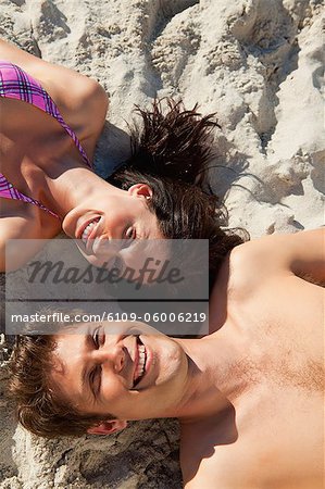 Portrait d'un couple allongé sur une plage de sable tout en portant des maillots de bain
