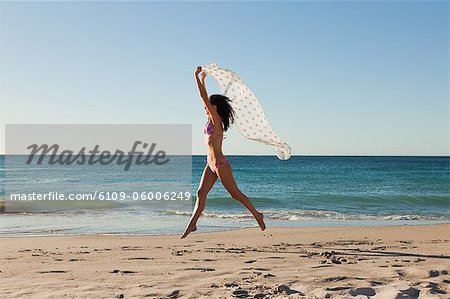 Attraktive Frau im Bikini am Strand direkt am Meer mit einem Sarong springen