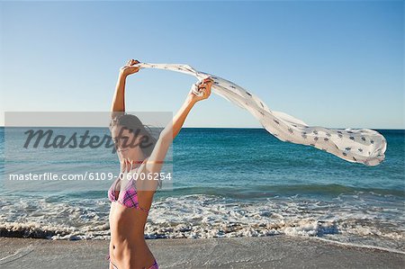 Young attractive woman holding her sarong in the air while standing on the beach