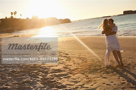 Sunset with a man raising his wife in the air on the beach