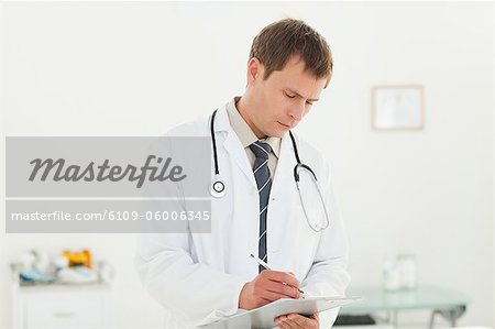 Young doctor taking notes on a clipboard in his examination room