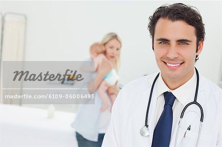 Smiling young doctor with woman and her baby standing behind him