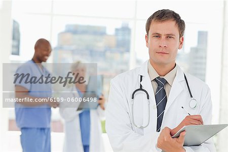 Doctor with clipboard and two colleagues behind him