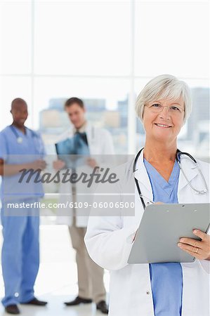 Mature doctor with clipboard and two colleagues behind her