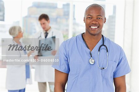 Smiling doctor in scrubs with two colleagues behind him